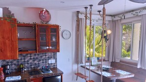 Una cocina con armarios de madera, un refrigerador, un lavamanos y un ventanal con cortinas.