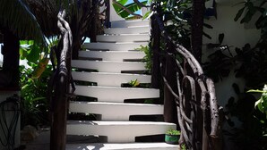 Una escalera blanca con barandillas de madera, rodeada de exuberante vegetación y un cielo azul despejado.