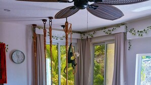 Una habitación con una mesa y banco de madera, un ventilador de techo, un reloj y una ventana con cortinas.