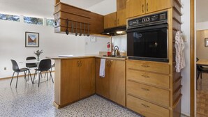 A compact kitchen with wooden cabinets, a built-in oven, and a dining area with a table and chairs. - Las Hermanas - Close to Sul ROss, Kokernot Park, Downtown (Alpine)
