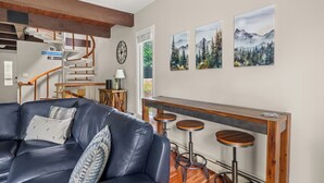 A modern living room with a leather sofa, a wooden staircase, and a bar area with stools.