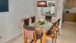 A modern dining area with a glass table and wooden chairs, a hanging pendant light, and a kitchen in the background. - Comfort & Relax! (El Dorado)