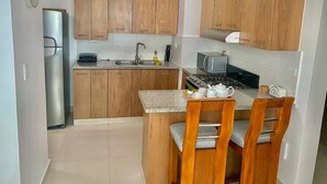 A compact kitchen with wooden cabinets, a refrigerator, a microwave, a stove, and a dining area with chairs. - Comfort & Relax! (El Dorado)