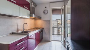 A compact kitchen with a gas stove, sink, and modern cabinetry. A clock is visible on the wall, and the room has a view of a balcony with buildings in the background. - Europa Landscape by Wonderful Italy (Catania)