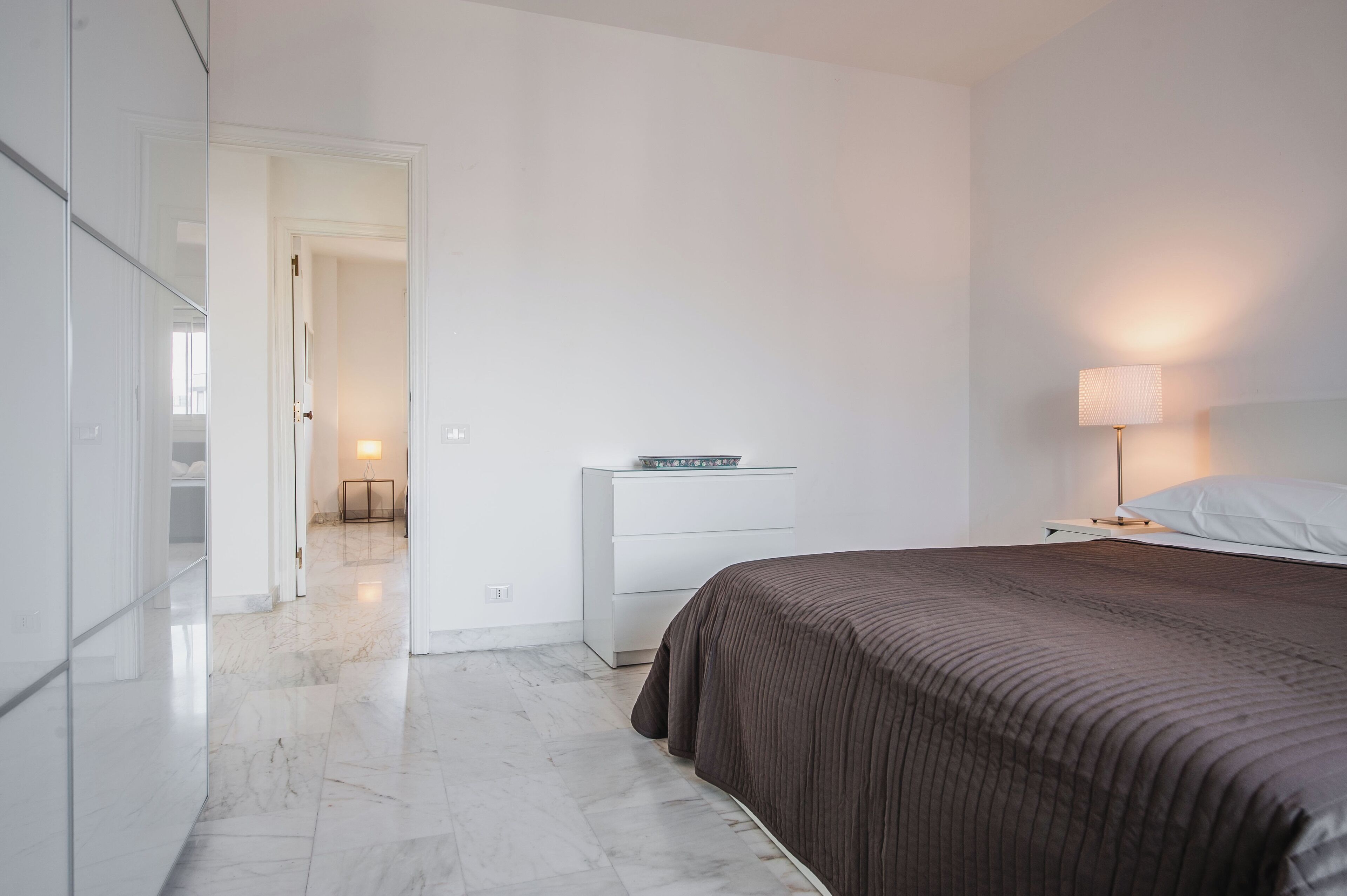Une chambre moderne avec un grand lit, une table de chevet avec une lampe et une armoire.