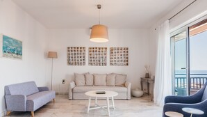 A modern living room with a sofa, a round coffee table, and a blue armchair. There is a large window with a view of the sea. - Europa Landscape by Wonderful Italy (Catania)