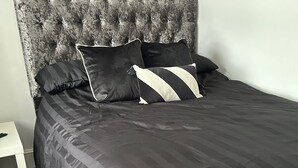 Un lit bien fait, avec une tête de lit capitonnée, une literie sombre et des oreillers à rayures.