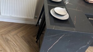 Une cuisine avec un plan de travail en marbre noir, deux assiettes blanches et un verre.