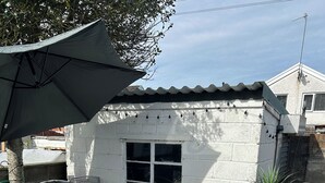 Une terrasse avec une table et des chaises, un pot de fleurs et un barbecue.
