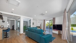 A modern living room with a teal sofa, wooden flooring, a TV, and a large window with curtains. - Villa Pinus with Pool, Game Room, Garden (Cervar Porat)