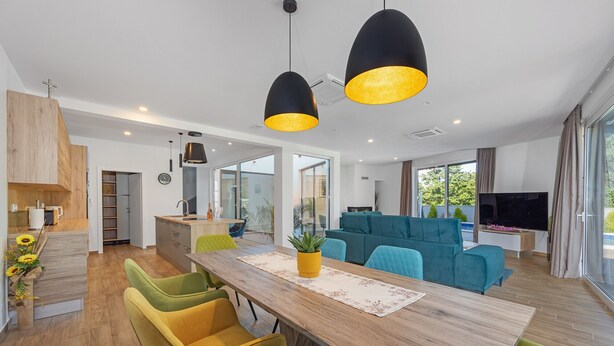 A modern living room with a wooden dining table, colorful chairs, and a large TV. - Villa Pinus with Pool, Game Room, Garden (Cervar Porat)