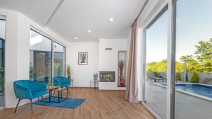 A spacious room with a large sliding glass door leading to a pool area, a small table with chairs, and a potted plant. - Villa Pinus with Pool, Game Room, Garden (Cervar Porat)
