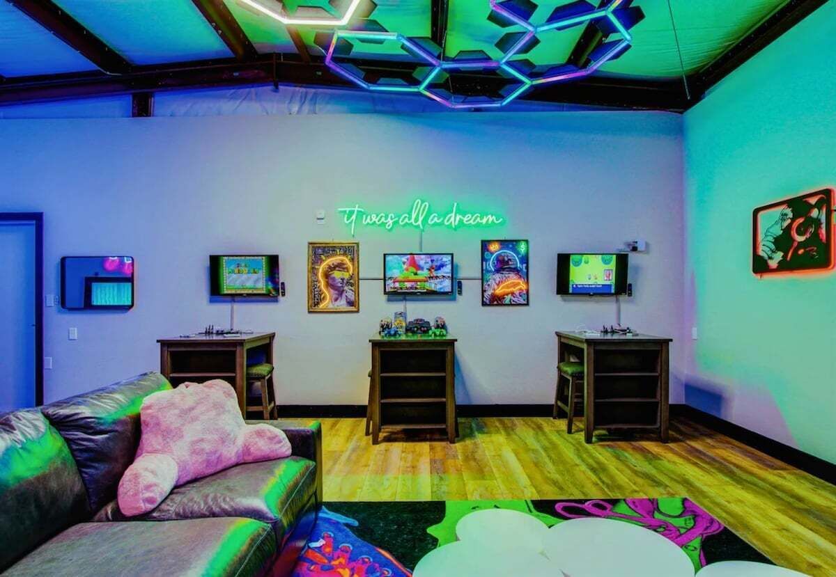 A room with a neon sign, a couch, a table, and artwork on the wall.