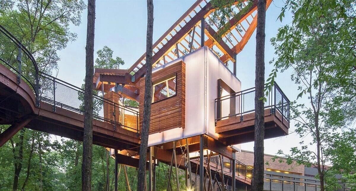 Ein Baumhaus mit Holzfassade, einem Balkon und einer Treppe.