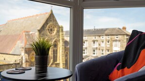 Une pièce avec vue sur un bâtiment historique, une table ronde ornée d’une plante en pot et un canapé recouvert d’une couverture.
