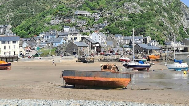 Une ville côtière avec des bâtiments construits sur une colline, des bateaux sur la plage et un paysage rocheux en arrière-plan.