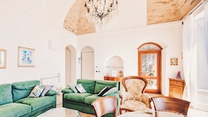 A living room with a green sofa, a wooden chair, a glass coffee table, and a chandelier. - Appartamento fronte mare a Ospedaletti by Wonderful Italy (Ospedaletti)