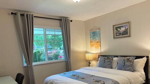 Une chambre à coucher comprenant un lit, un bureau, une chaise, une fenêtre avec des rideaux, une lampe et deux œuvres d’art murales.