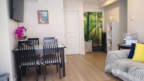 Un espace de vie compact comprenant un coin repas, un canapé et un tableau représentant un paysage côtier.