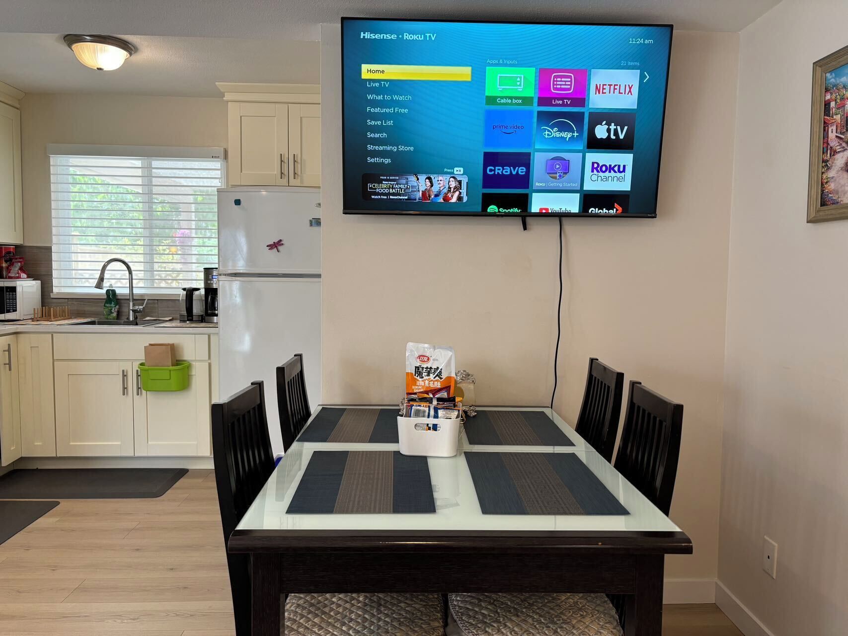 Une cuisine moderne avec un coin repas, un téléviseur à écran plat fixé au mur qui affiche l’interface d’un service de diffusion en continu, et une table avec un sac de collations.