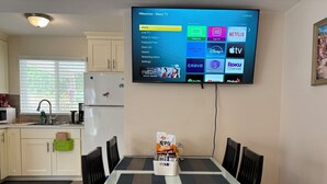 Une cuisine moderne avec un coin repas, un téléviseur à écran plat fixé au mur qui affiche l’interface d’un service de diffusion en continu, et une table avec un sac de collations.