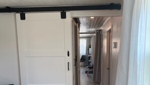 Un couloir avec une porte coulissante, une chaise noire et une fenêtre avec des rideaux.