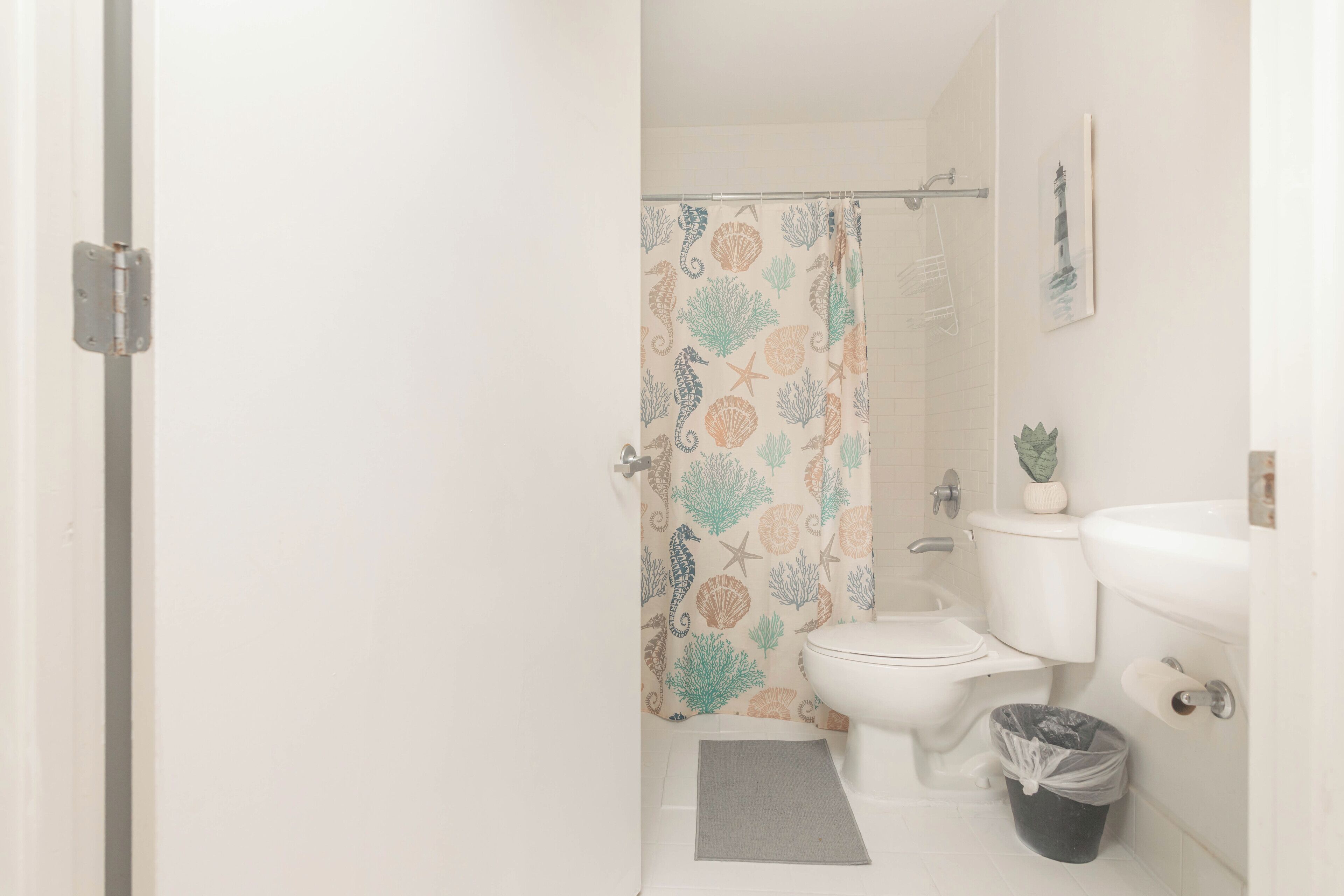Een badkamer met toilet, wastafel, douchegordijn met een schelpenprint en een kleine potplant.
