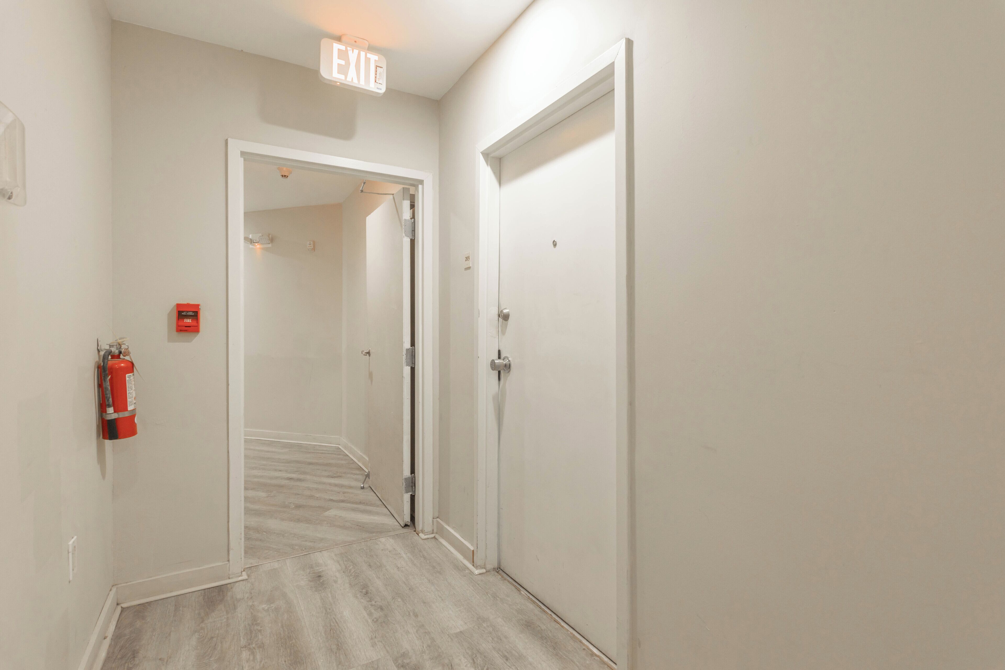 A hallway with a fire extinguisher, an exit sign, and a door.