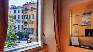 A room with a window overlooking a street, a bookshelf with books, and a radiator. - La finestra sul cortile di Via Roma by Wonderful Italy (Genoa)