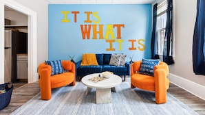 Un salon avec un mur bleu, deux fauteuils orange, un canapé bleu et une table basse.