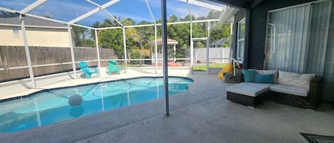 Un patio couvert avec une piscine, des sièges d’extérieur et une vue sur le jardin arrière.