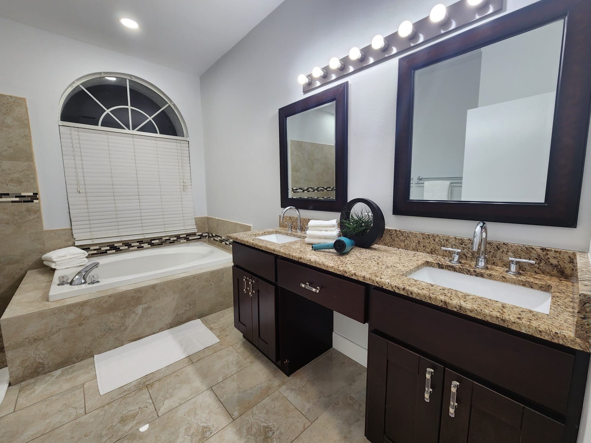 A modern bathroom with a bathtub, two sinks, and a vanity with dark cabinets.