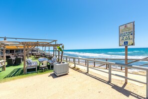 Un restaurante frente a la playa con terraza, un letrero que indica acceso a la playa pública y vistas al océano.