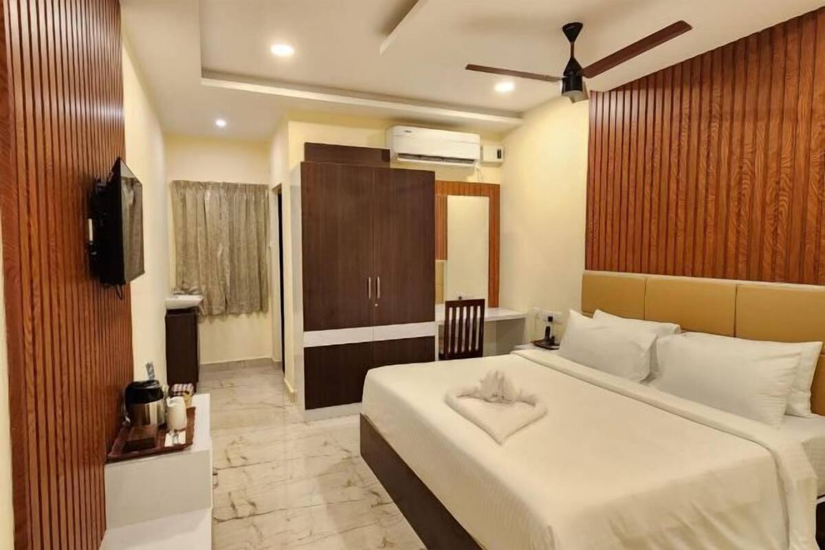 A hotel room with a bed, a desk, a chair, a television, and an air conditioning unit.