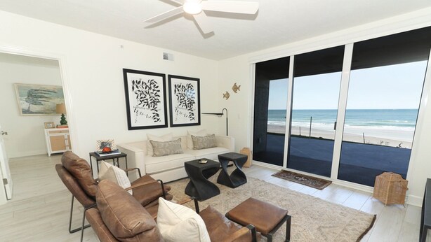 A modern living room with a leather sofa, a coffee table, and a large window overlooking the beach.