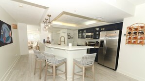 A modern kitchen with a central island, stainless steel appliances, and a seating area with wicker chairs.