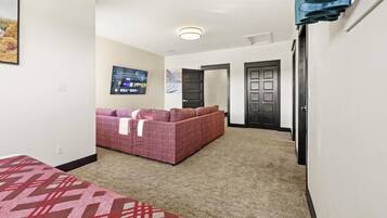 A hotel room with a large bed, a sofa, a TV, and a carpeted floor.