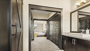Een gang die leidt naar een slaapkamer met een grote kast en een badkamer met een wastafel en spiegel.