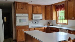 A kitchen with wooden cabinets, a white island, and a window with a red valance. - Quiet Country Home on 10 acers of land, located only 23 miles from EAA grounds. (Larsen)