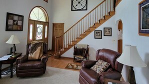 A spacious living room with a wooden staircase, leather sofas, and a large clock on the wall. - Quiet Country Home on 10 acers of land, located only 23 miles from EAA grounds. (Larsen)