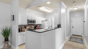 A modern kitchen with white cabinetry, a central island, and a microwave. - Newly Renovated Condo Minutes from The Beach, OWA Water Park and Tanger Outlets (Foley)