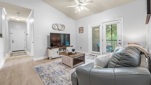 A living room with a ceiling fan, a TV, a wooden coffee table, and a gray leather couch. - Newly Renovated Condo Minutes from The Beach, OWA Water Park and Tanger Outlets (Foley)