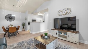 A modern living room with a TV, dining table, and chairs. - Newly Renovated Condo Minutes from The Beach, OWA Water Park and Tanger Outlets (Foley)