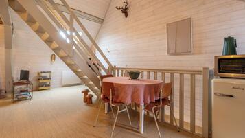 Une pièce avec un escalier, une table ronde entourée de chaises, un petit réfrigérateur et une tête de cerf fixée au mur.
