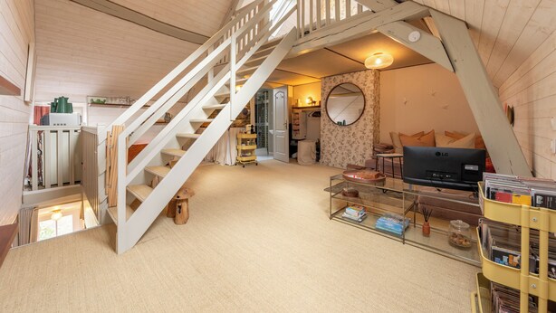Una stanza in stile loft con una scala in legno, una televisione e una libreria.