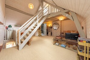A loft-style room with a wooden staircase, a television, and a bookshelf. - Cottage de Charme " les Hirondelles " (Samois-sur-Seine)
