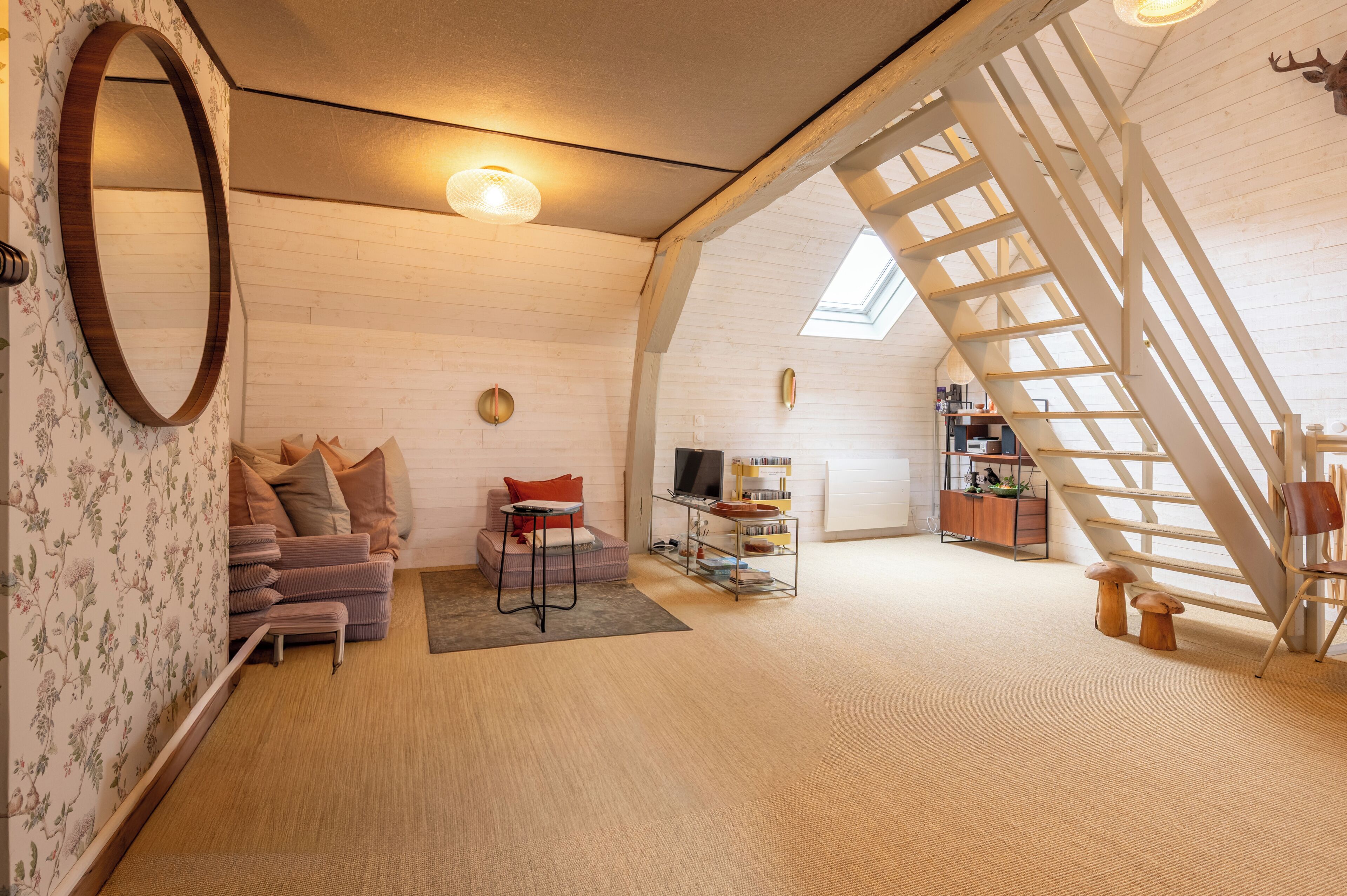 A loft-style room with a wooden ceiling, a sofa, a small table, a TV, and a bookshelf.