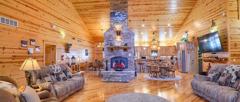 A log cabin interior with a stone fireplace, wooden furniture, and a television.
