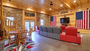 A wooden interior with a stone wall, a staircase, a seating area, and an American flag. - Freedom Lodge by Turkey Ridge Lodges (Rockbridge)