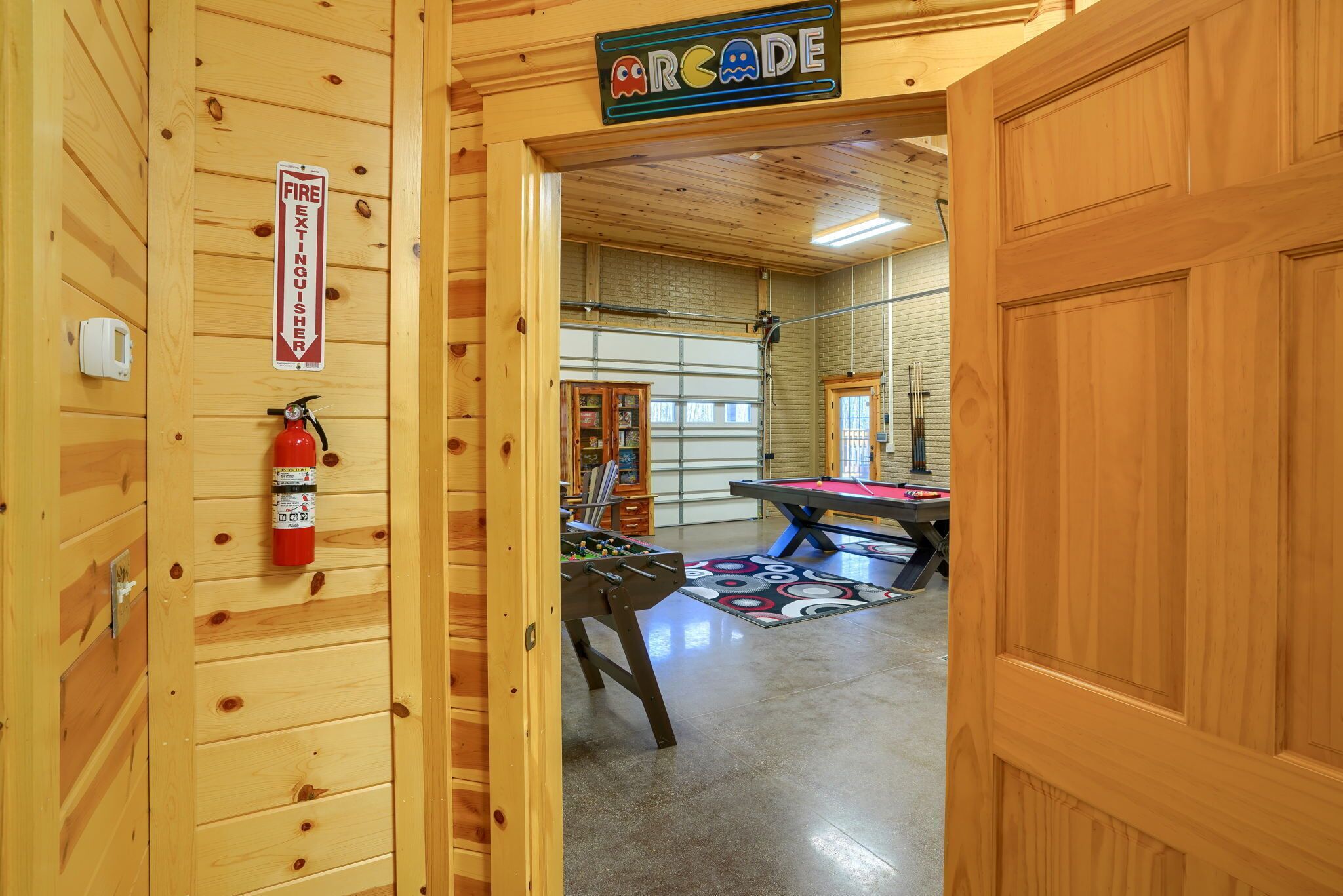 Una habitación con piso de madera, mesa de billar, mesa de fútbol de mesa y un extintor de incendios montado en la pared.